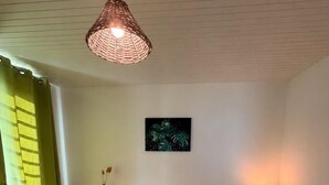 Et soveværelse med en seng, et natbord, en lampe, et billede på væggen og en pendel.