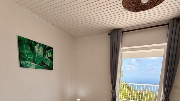 Et soveværelse med seng, natbord, lampe, et billede og en balkon med udsigt.