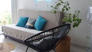 Et værelse med sofa, sort stol, plante og ventilator.