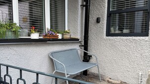 Een balkon met een metalen stoel, planten in potten en een raam met zonwering.