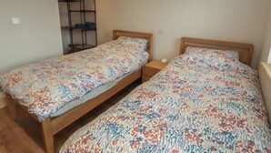Een slaapkamer met twee eenpersoonsbedden, een houten hoofdbord, een nachtkastje met een lamp en een inbouwplank.