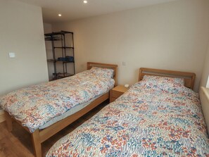 Ein Schlafzimmer mit zwei Einzelbetten, einem Holz-Kopfstück, einem Nachttisch mit Lampe und einer eingebauten Schrankwand.