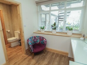 Et badeværelse med toilet, en trädør, en stol og et vindue med persienner og plantepotte.