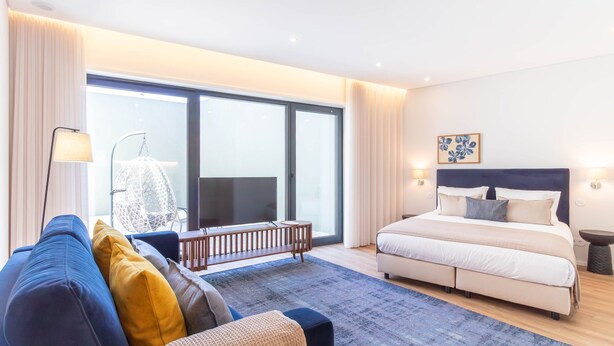 Una habitación de hotel moderna con una cama grande, un sofá, un televisor y vistas por una ventana amplia.
