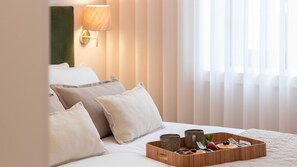 A hotel room with a bed, pillows, a tray with breakfast items, and a wall-mounted lamp. - 1F | Rosário 244 by LovelyStay (Porto)