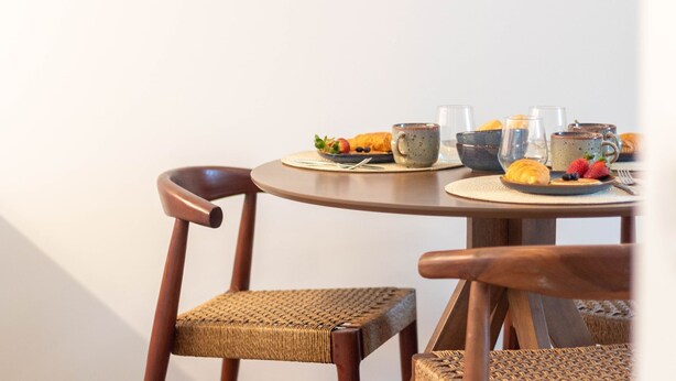 A round dining table with a woven chair, a plate of fruit, and a cup. - 1T | Rosário 244 by LovelyStay (Porto)