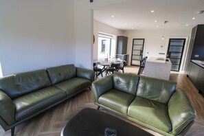 A modern living room with two green leather sofas, a black ottoman, and a dining area with a table and chairs. - AN TOBAR, family friendly, with a garden in Belmullet, County Mayo (Ballina)
