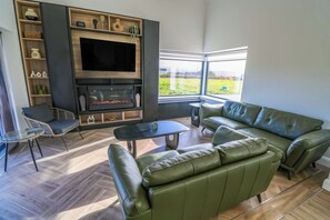 A modern living room with a fireplace, green leather sofa, and a glass coffee table.