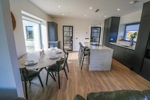 A modern kitchen with a dining area, wooden flooring, and a view through a glass door. - AN TOBAR, family friendly, with a garden in Belmullet, County Mayo (Ballina)