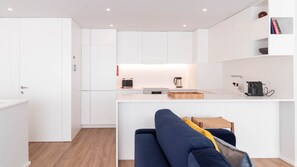 A modern kitchen with white cabinetry, a built-in island, and a seating area with a blue sofa. - 2F | Rosário 244 by LovelyStay (Porto)
