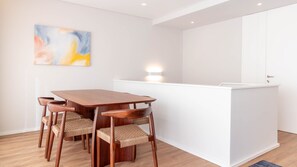 A modern kitchen with a wooden table and woven chairs, a white island, and a painting on the wall. - 2F | Rosário 244 by LovelyStay (Porto)
