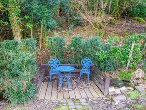 Eine Holzterrasse mit Tisch und Stühlen, umgeben von viel Grün.