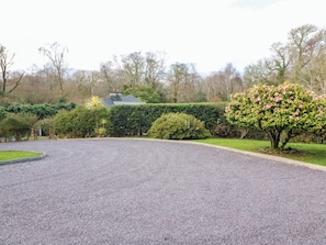 Ein Kiesweg führt zu einem Haus mit einer gepflegten Hecke und einem blühenden Baum.