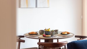 Une table ronde où l’on a disposé des assiettes remplies de nourriture, des tasses et un saladier de fruits.