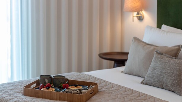 Un lit bien fait, avec un plateau en bois contenant des articles pour le petit-déjeuner, une table de chevet et une lampe.