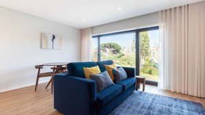 Un salon moderne avec un canapé bleu, une petite table ronde et une vue sur la verdure grâce à de grandes fenêtres.