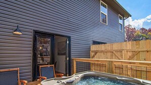 A hot tub in a backyard with a wooden deck, a chair, and a fence. - Cute Condo | Hot Tub | Minutes to Pigeon Forge! (Sevierville)