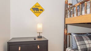 A bed with a plaid blanket, a bedside lamp, a nightstand with drawers, and a bear crossing sign on the wall. - Cute Condo | Hot Tub | Minutes to Pigeon Forge! (Sevierville)