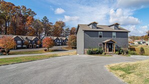 A two-story building with a dark exterior, a front entrance with a porch, and a driveway leading to a parking area. - Cute Condo | Hot Tub | Minutes to Pigeon Forge! (Sevierville)