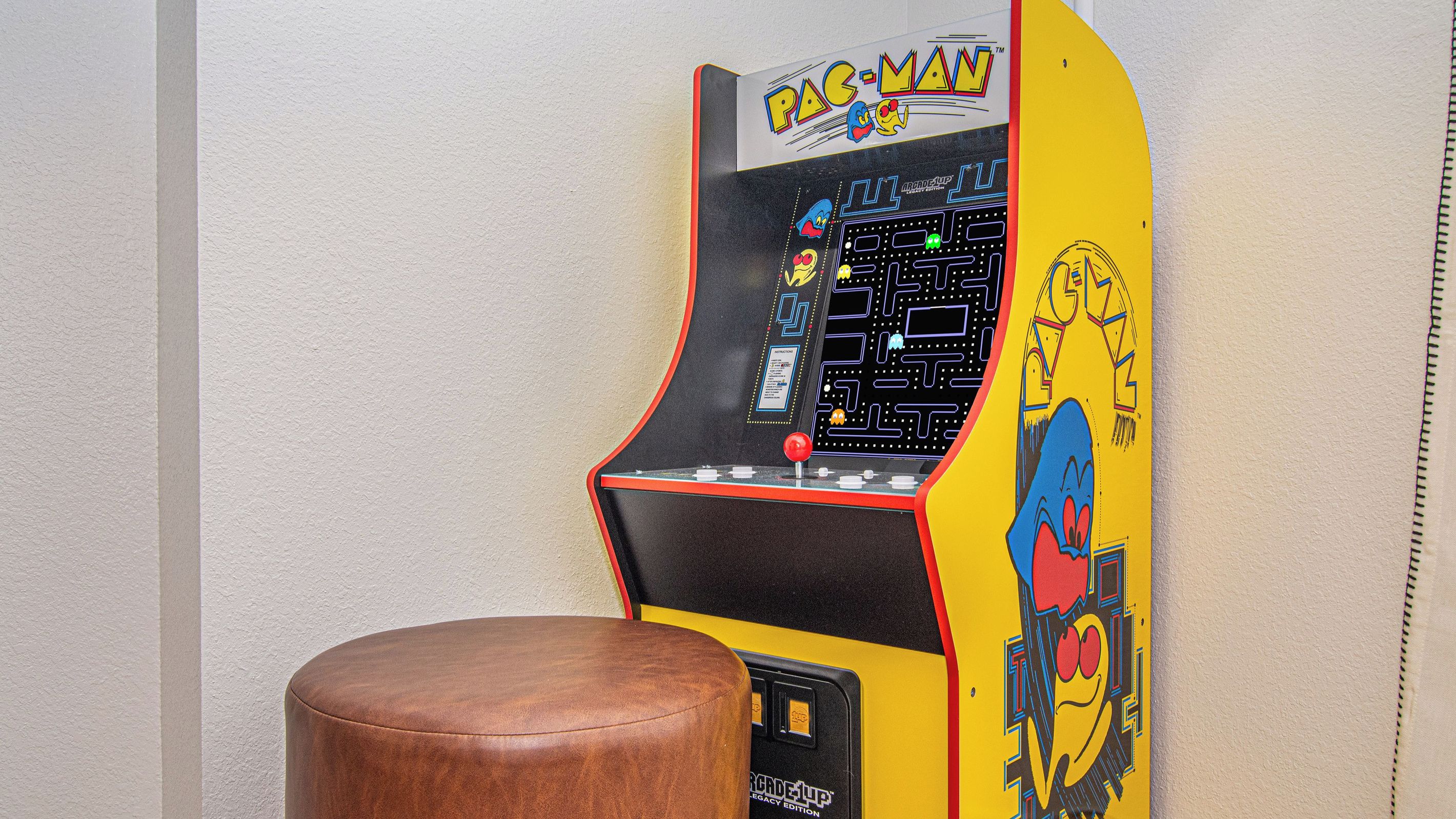 A Pac-Man arcade machine with a brown stool in front.