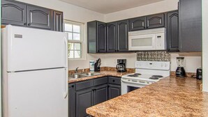 A kitchen with dark cabinets, a white refrigerator, a microwave, a stove, and granite countertops. - Cute Condo | Hot Tub | Minutes to Pigeon Forge! (Sevierville)