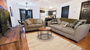 A living room with two sofas, a coffee table, and a rug. There is a kitchen in the background. - Cute Condo | Hot Tub | Minutes to Pigeon Forge! (Sevierville)