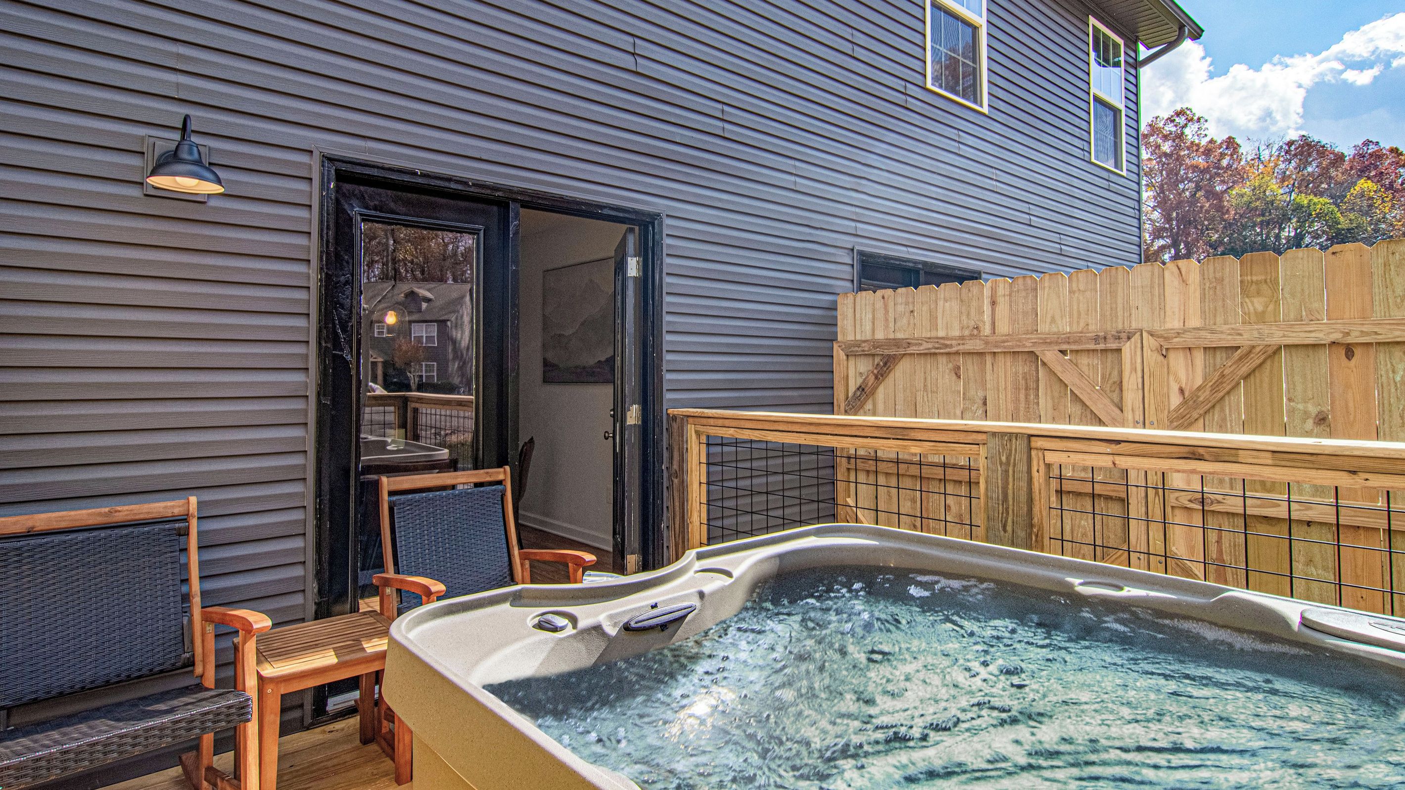 Ein Whirlpool mit einer Holzterrasse, einem Holenzaun und einem Haus mit Außenverkleidung.