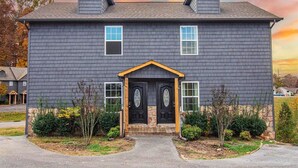 A two-story house with a dark gray exterior, a central entrance with a black door, and two small dormer windows on the roof. - Cute Condo | Hot Tub | Minutes to Pigeon Forge! (Sevierville)