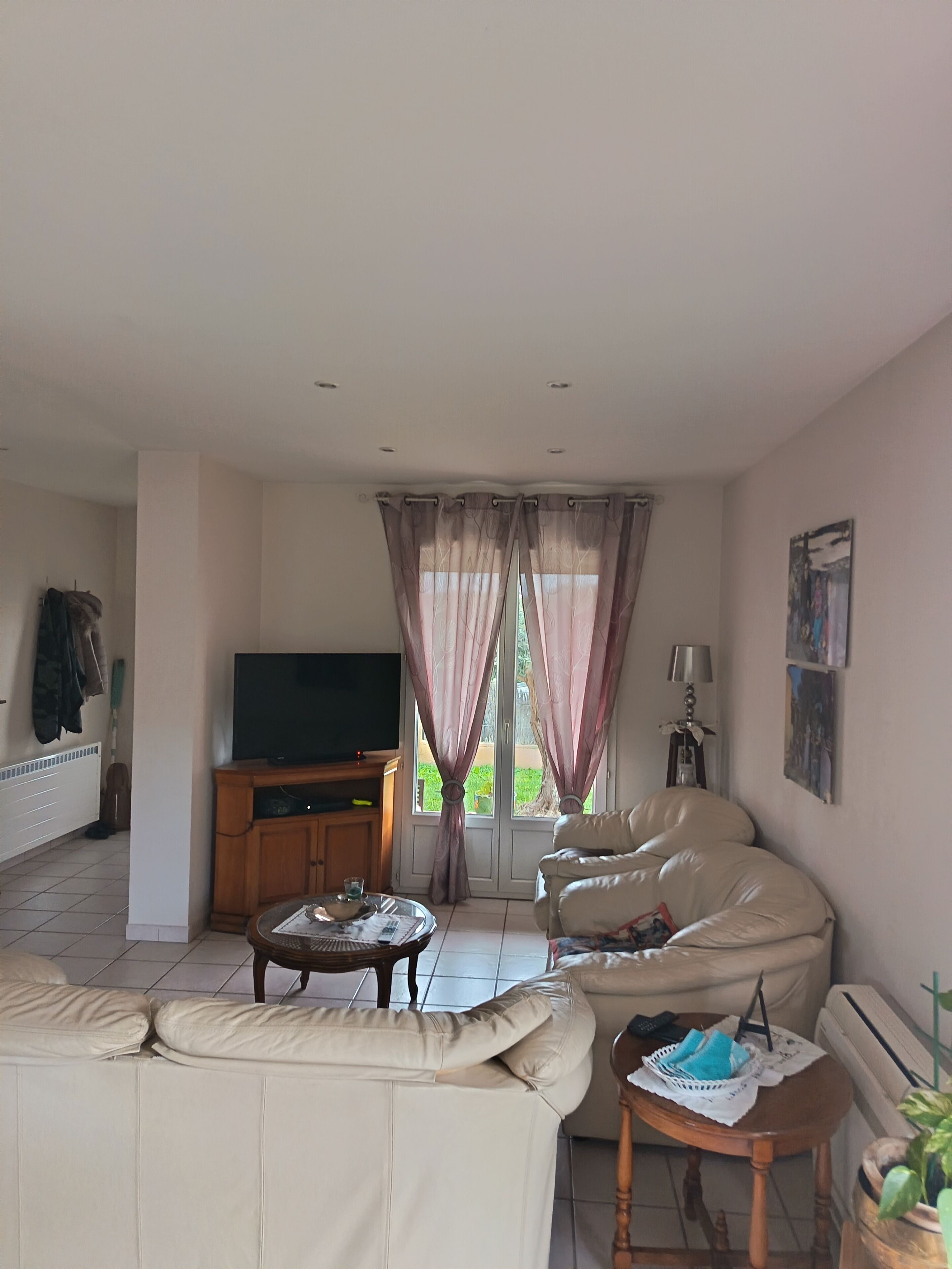 Ein Wohnzimmer mit einer Couch, einem Couchtisch, einem Fernseher und einem Fenster mit Vorhängen.