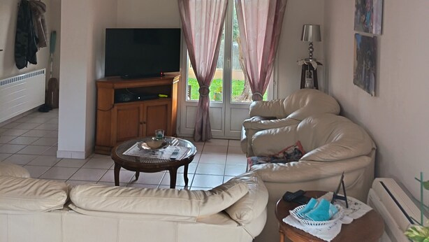 Ein Wohnzimmer mit einer Couch, einem Couchtisch, einem Fernseher und einem Fenster mit Vorhängen.