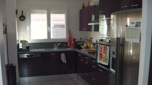 Eine Küche mit dunklen Schränken, einem Edelstahlkühlschrank, einem Fenster mit Blick und einem Fliesenboden.