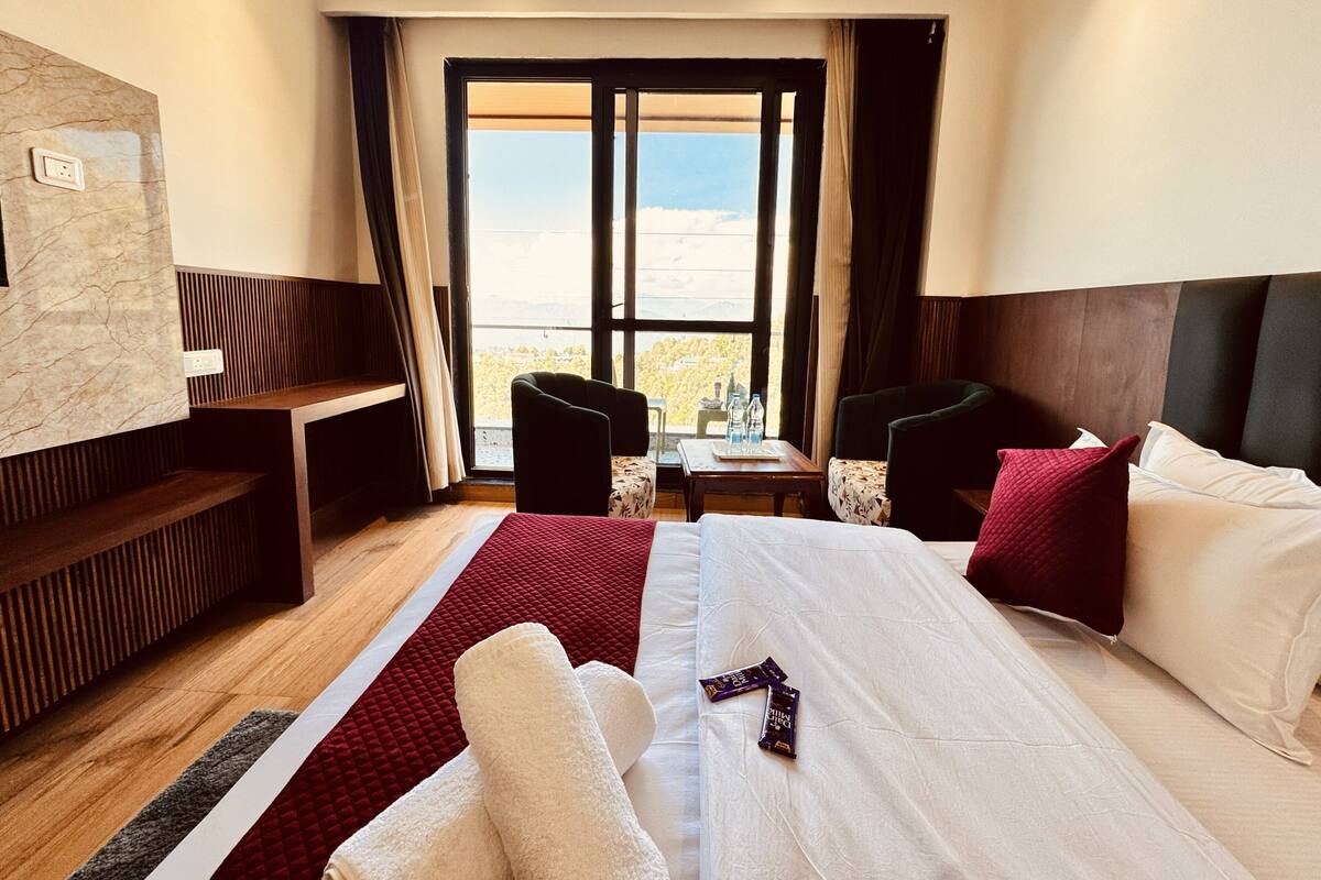 A hotel room with a large bed, a desk, a chair, and a view of the outdoors.