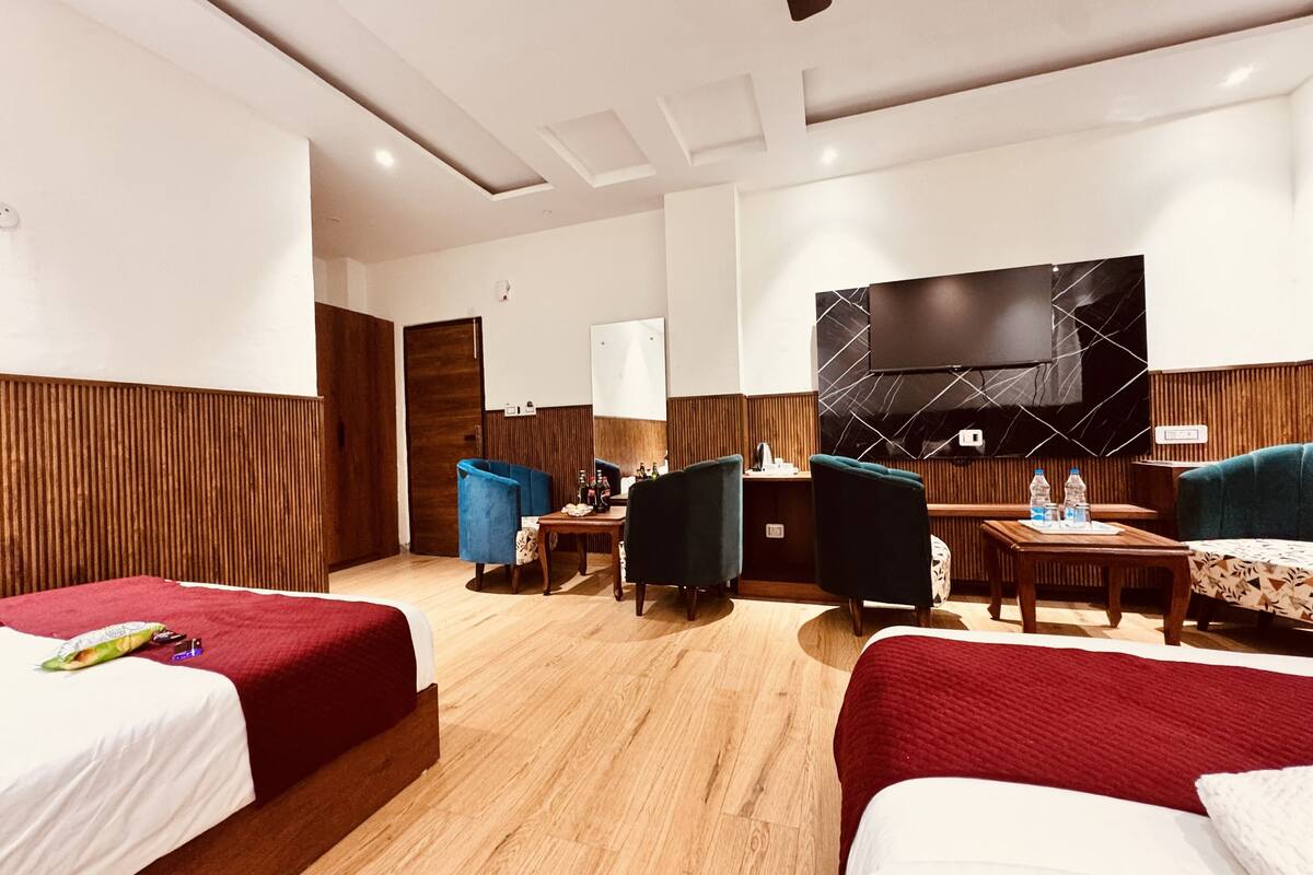 A hotel room with two beds, a desk, chairs, a TV, and a wooden panel wall.