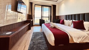 Moderni hotellihuone, jossa on sänky, seinälle asennettu televisio, kattotuuletin ja näkymä ikkunasta.