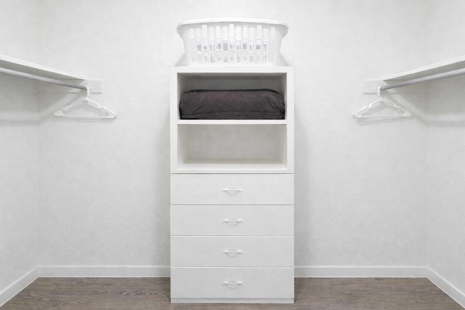 Un placard blanc avec un panier suspendu, une étagère et quatre tiroirs.