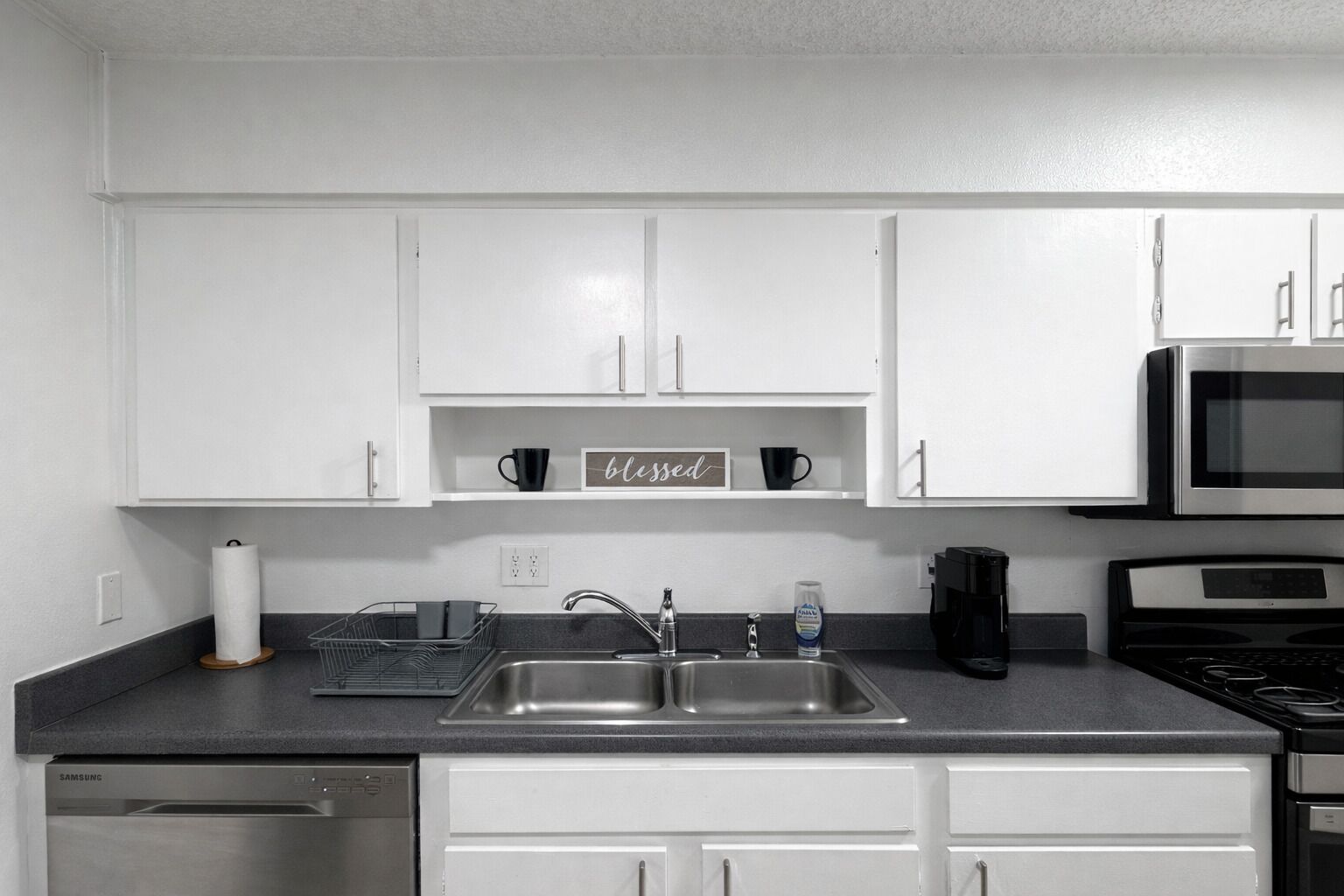 Una cucina moderna con mobili bianchi, un lavello in acciaio inossidabile, un forno a microonde e una macchina da caffè.