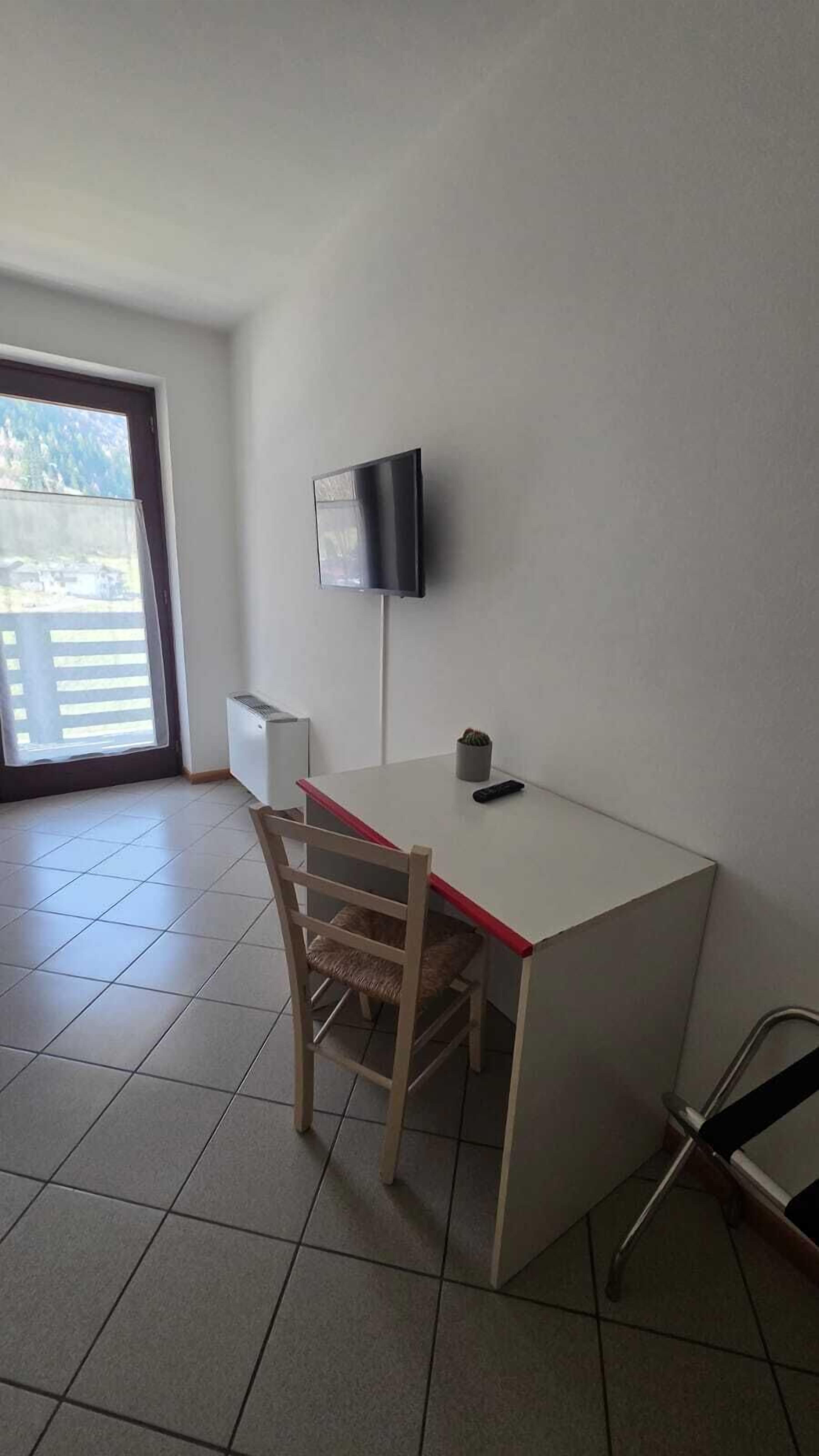 A small, clean room with a desk, chair, TV, and a window with a view.