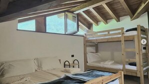 A wooden ceiling with a sloped roof, a bunk bed, a single bed, and a window. - Albergo Ristorante Casa Corti (Valbondione)