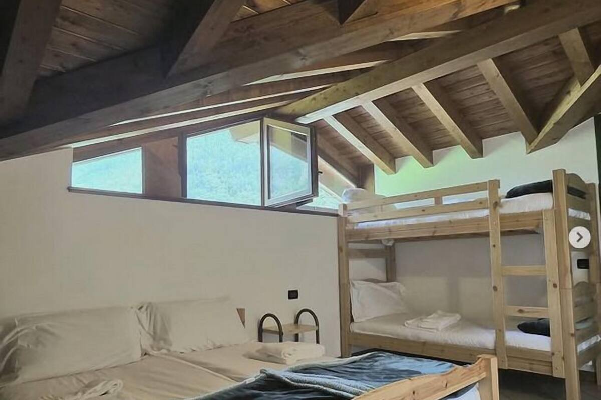 A wooden ceiling with a sloped roof, a bunk bed, a single bed, and a window.
