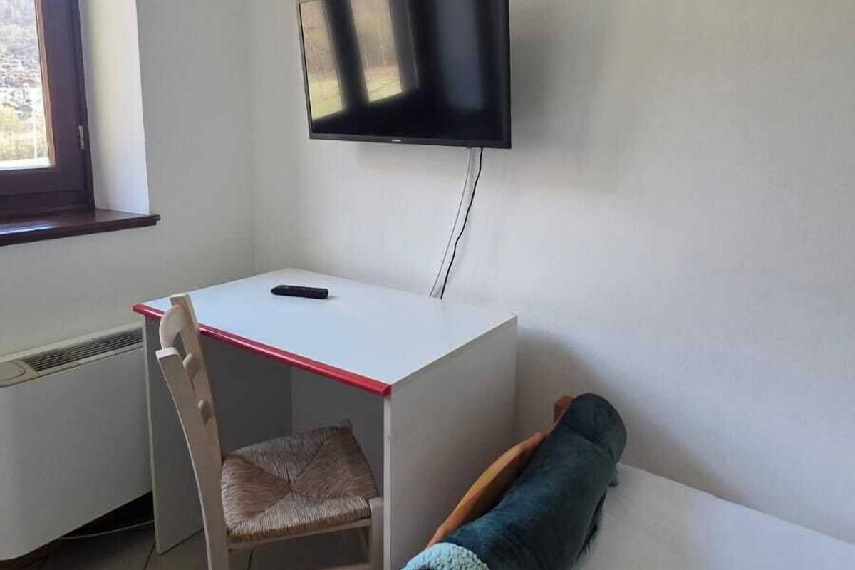 A room with a bed, a desk with a chair, a television mounted on the wall, and a window.