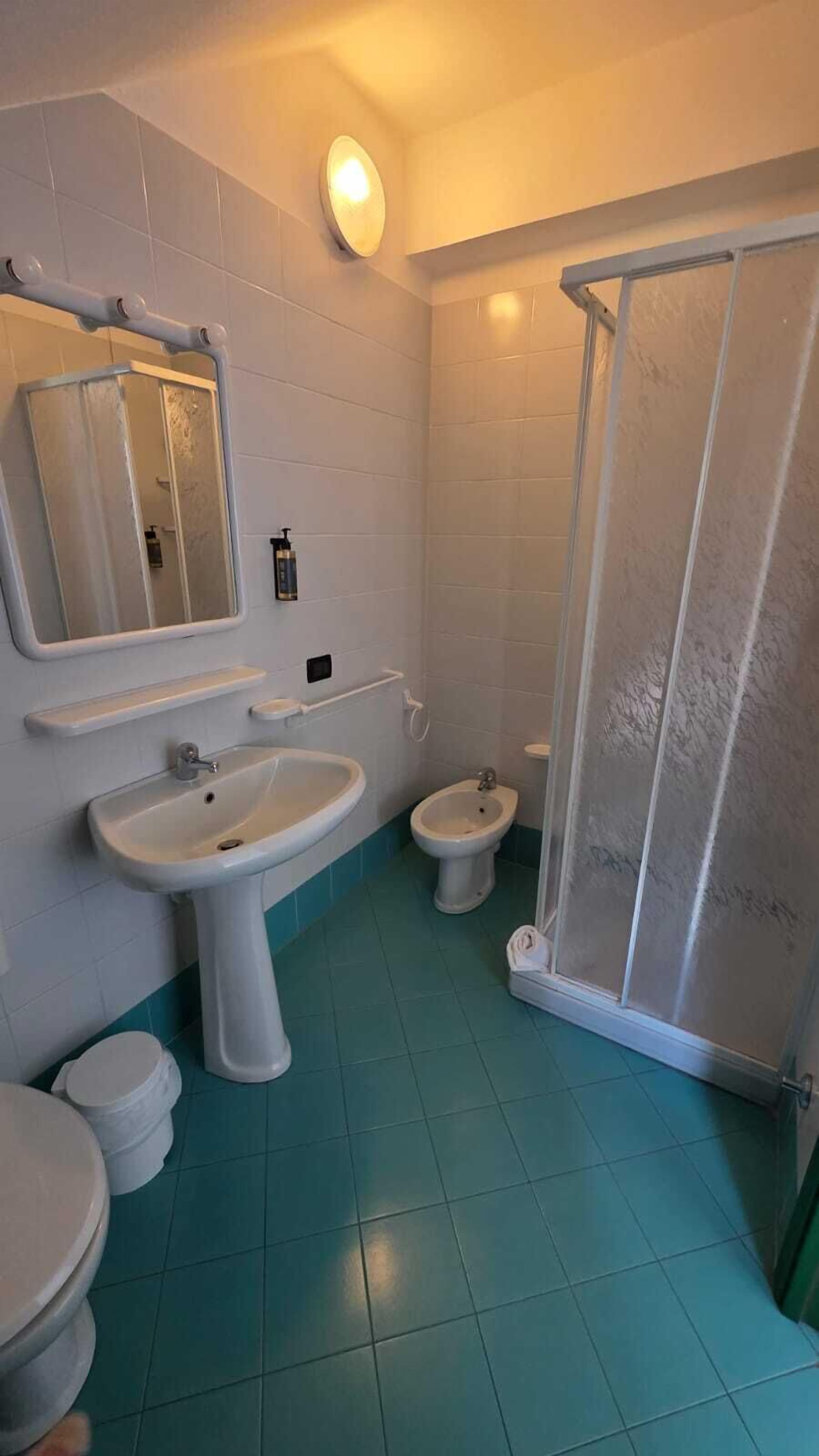 Un bagno con doccia, due lavandini, un water e uno specchio.