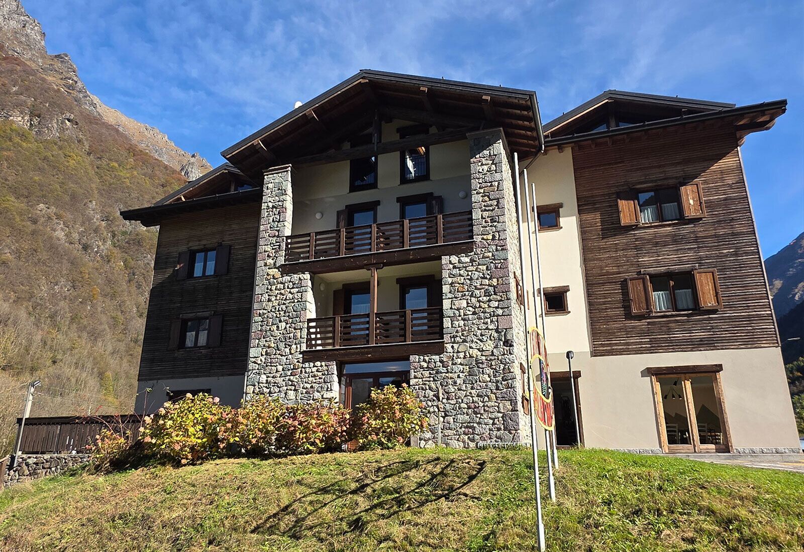 A multi-story building with a stone facade, balconies, and a mountain backdrop.