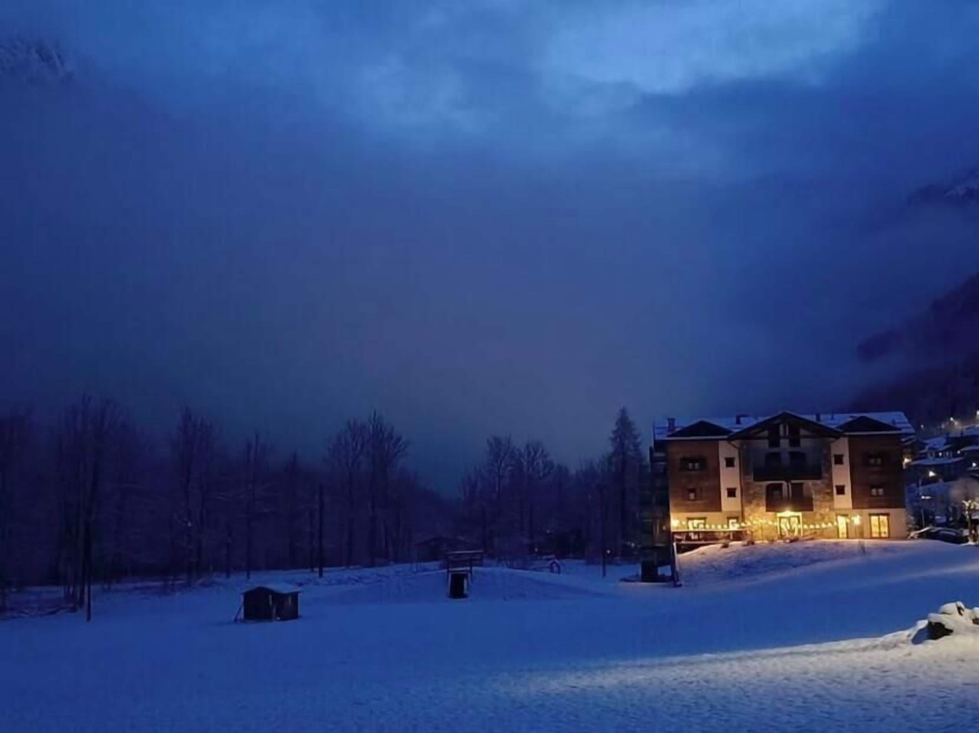A multi-story building with a snow-covered ground, surrounded by trees and a mountainous backdrop.