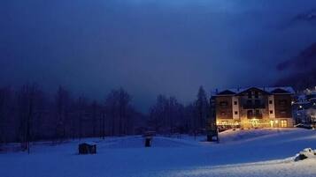 A multi-story building with a snow-covered ground, surrounded by trees and a mountainous backdrop.