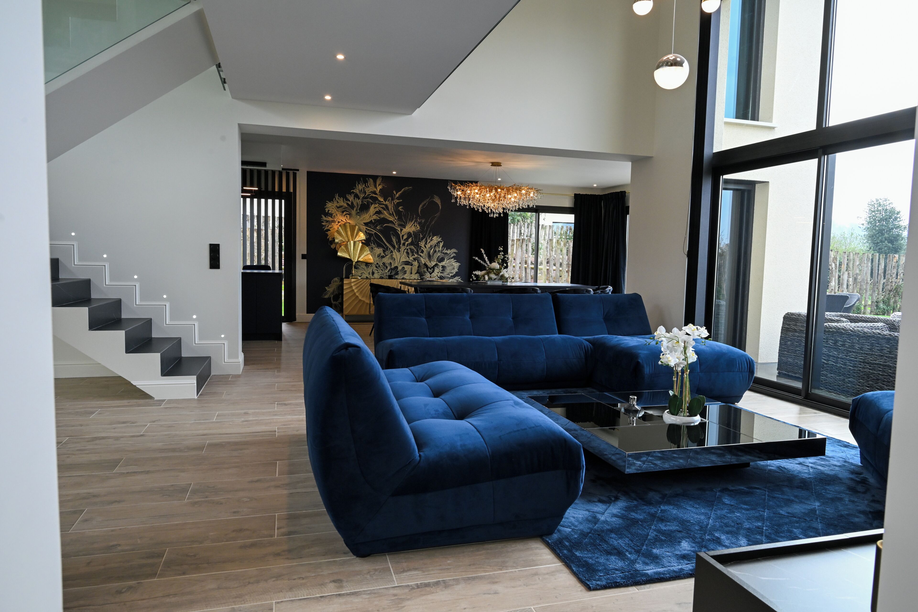 A modern living room with a staircase, a large sofa, a coffee table, and a chandelier.