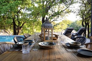 An outdoor dining table with chairs, a lantern, and a pool in the background. - Villa Riviersig,  a new stylish bushvilla (Hoedspruit)