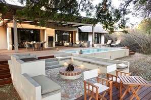 Un área de piscina moderna al aire libre, con un jacuzzi integrado, asientos y una chimenea.