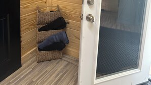 Une pièce avec un mur en bois, une porte blanche dotée d’une moustiquaire et un panier en osier contenant des vêtements.