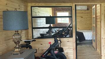 A wooden room with a bed, a desk with a lamp, and a Peloton exercise bike.