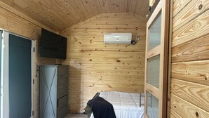 Une pièce aux murs lambrés, comprenant un lit, une commode et un climatiseur fixé au mur.